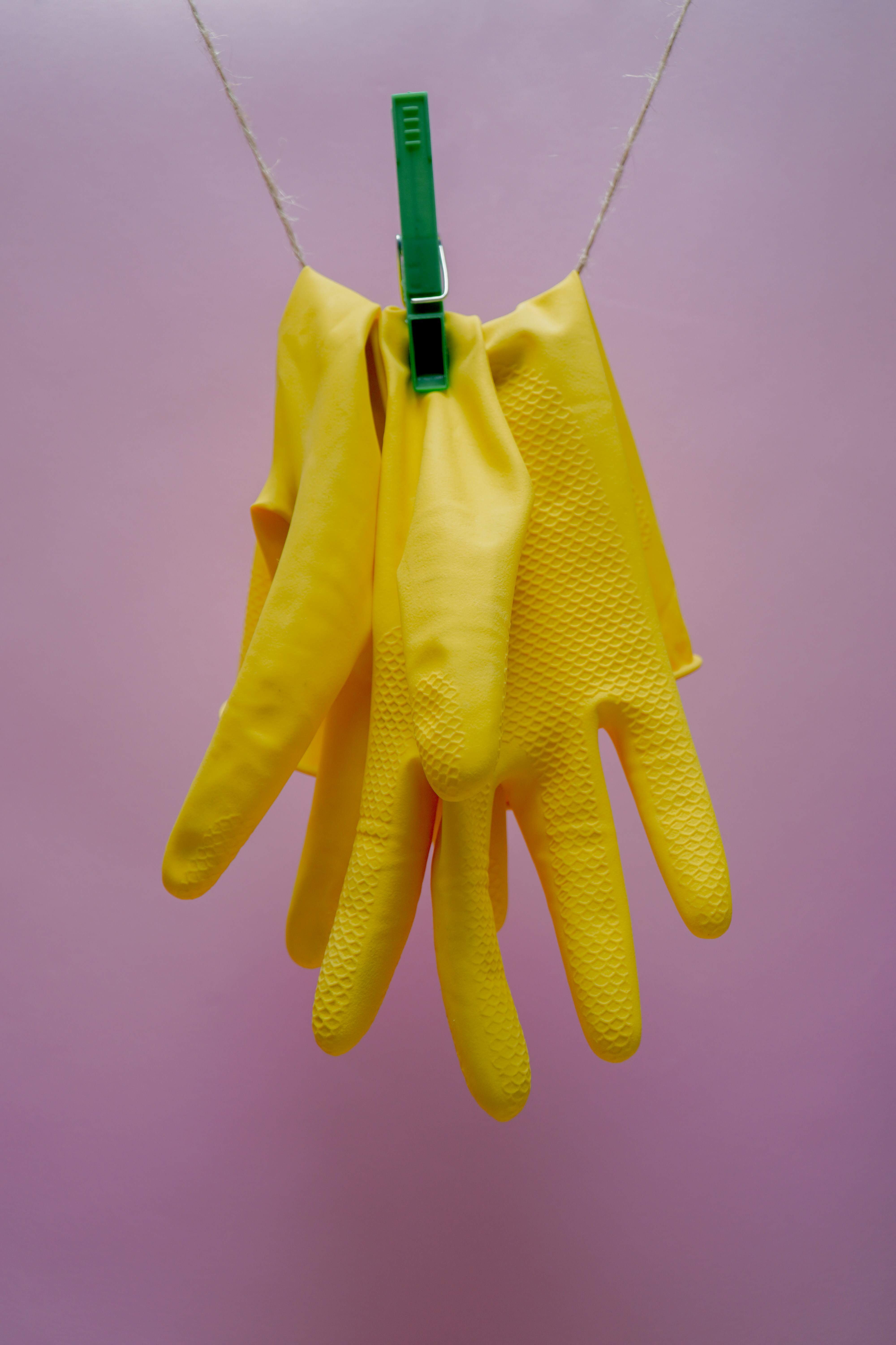 Gelbe Gummihandschuhe hängen mit grüner Wäscheklammer an Leine vor rosa Hintergrund